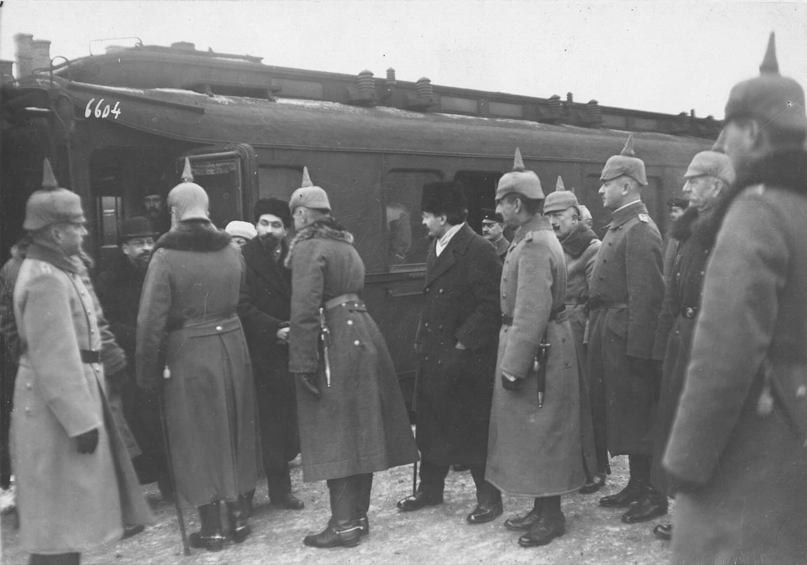 Deutsche Offiziere mit Pickelhauben empfangen Männer in Zivilmänteln vor einem Eisenbahnwagen im Schnee